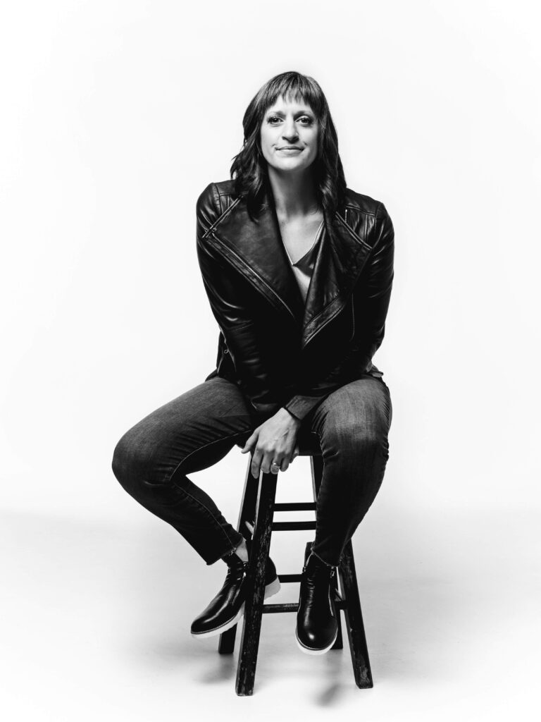 black & white photo of caryn sitting on a stool wearing a black leather jacket