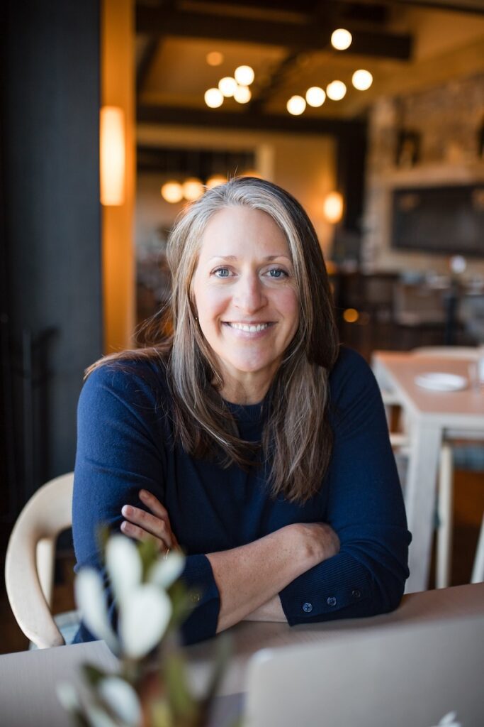Caryn at a table with arms folded.