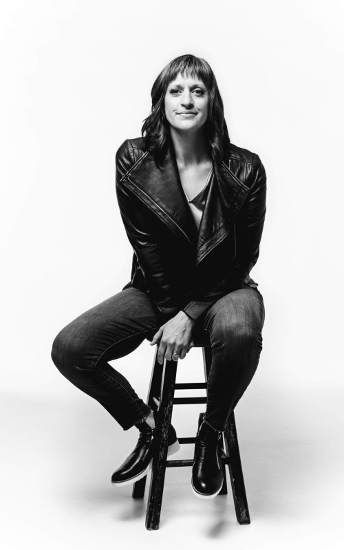 black & white photo of caryn sitting on a stool wearing a black leather jacket